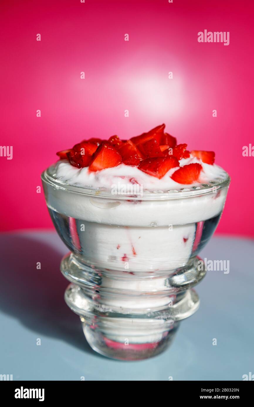 Ready-to-eat strawberry yogurt in a crystal glass on a pink and blue background Stock Photo