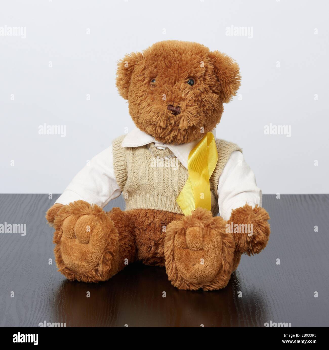 brown teddy bear sits and a yellow silk ribbon on a black wooden background, concept of the fight against childhood cancer, problem of suicides and th Stock Photo