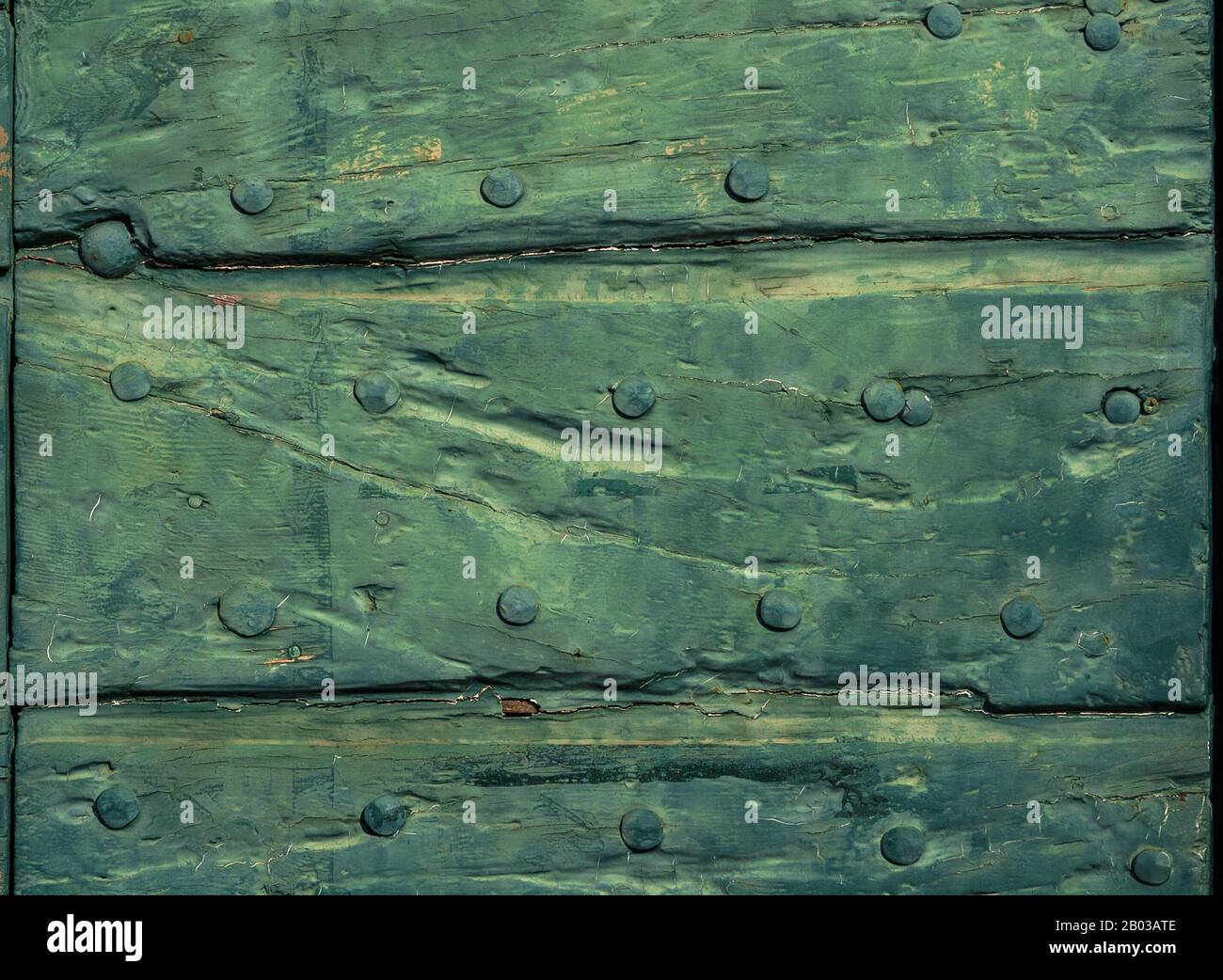 Old wooden door with green varnish, cracks and iron studs as background