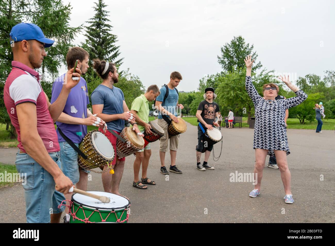 Krasnoyarsk, Russia, June 30, 2019: Adult woman funny dancing in front of men playing African drums Tam Tam djembe in a public Park in the summer. Stock Photo