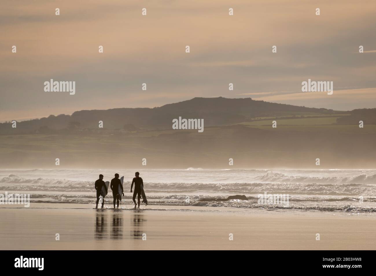 Surfers carrying their boards on the beach at Godrevy, Cornwall, UK Stock Photo