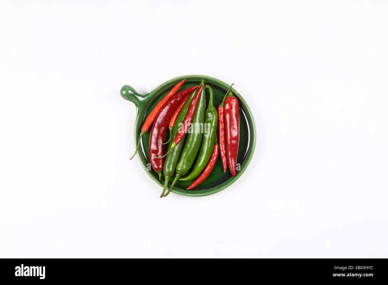 Close up of red and green hot chili peppers on green plate flat lay, white background. Stock Photo