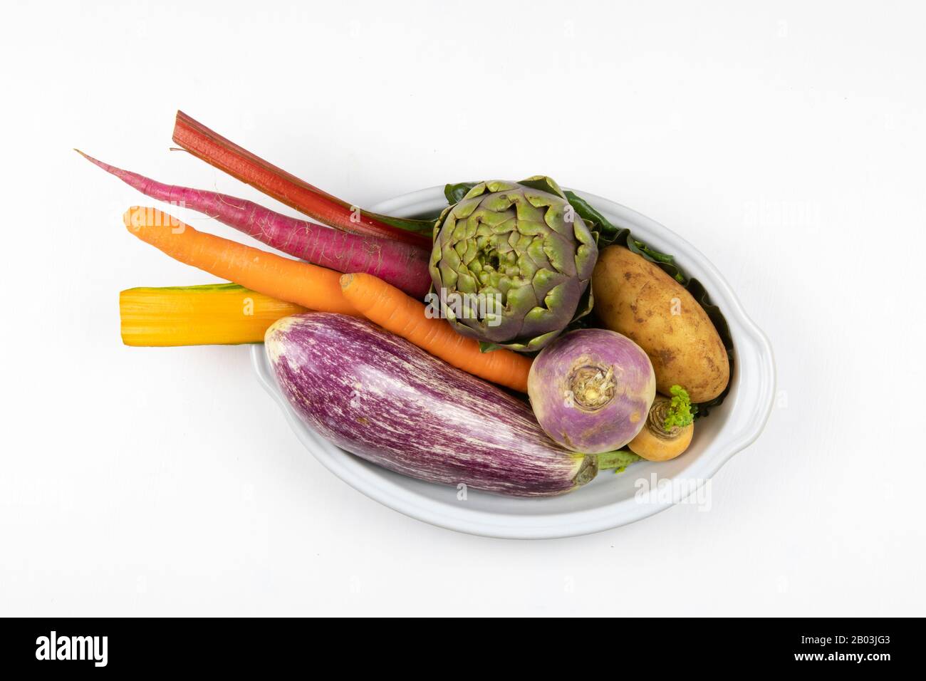 Composition of purple, orange and green vegetables in baking dish. Eggplant, potato, artichoke, carrot, colorful raw vegetables still life Stock Photo