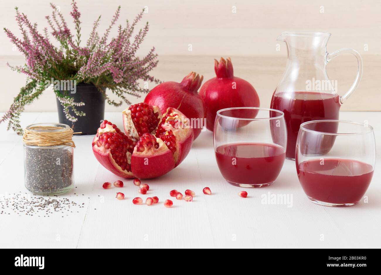 2 glasses and pitcher of fresh pomegranate juice, few ripe pomegranates with one partially peeled pomegranate. Rouge pomegranate seeds and jar of chia Stock Photo