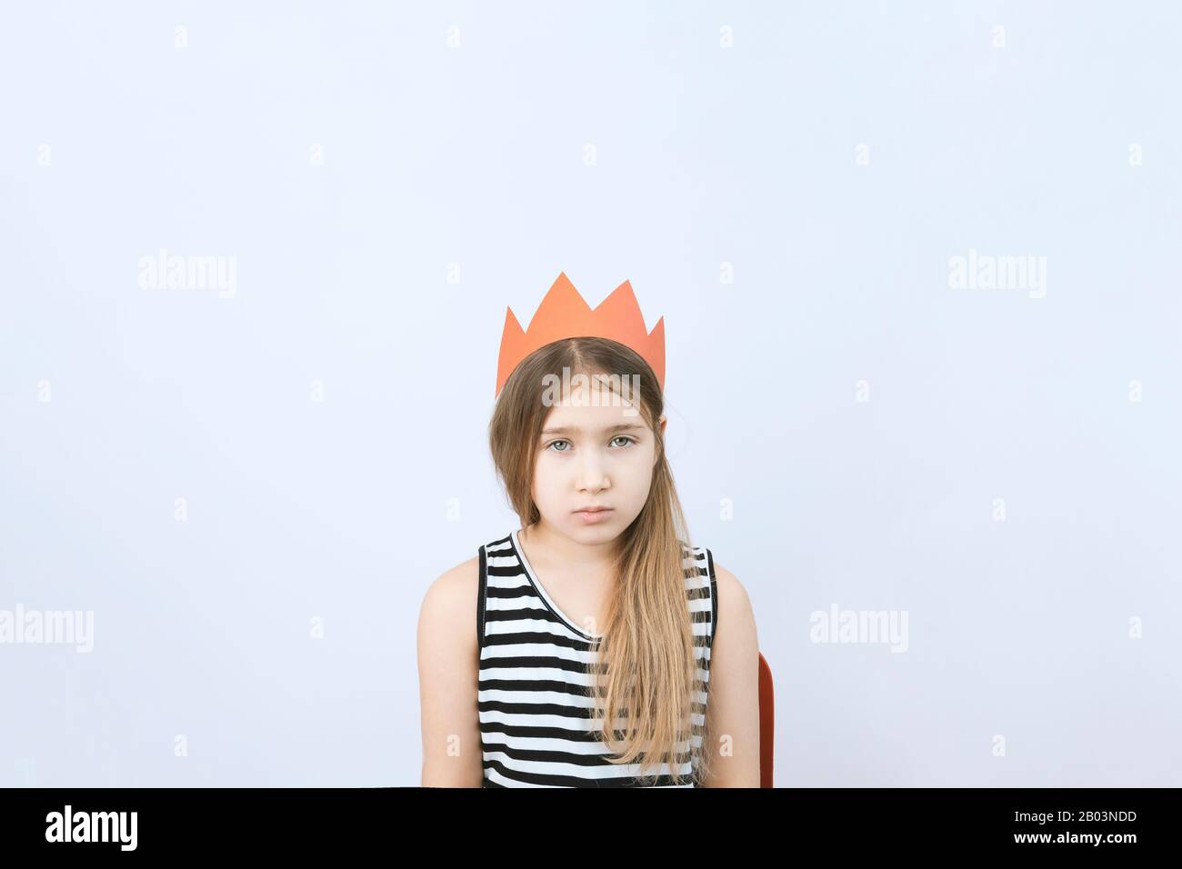 Sad young teenager girl in red crown on gray background. Sadness, megalomania and depression concept for psychologist and psychotherapist. Stock photo Stock Photo