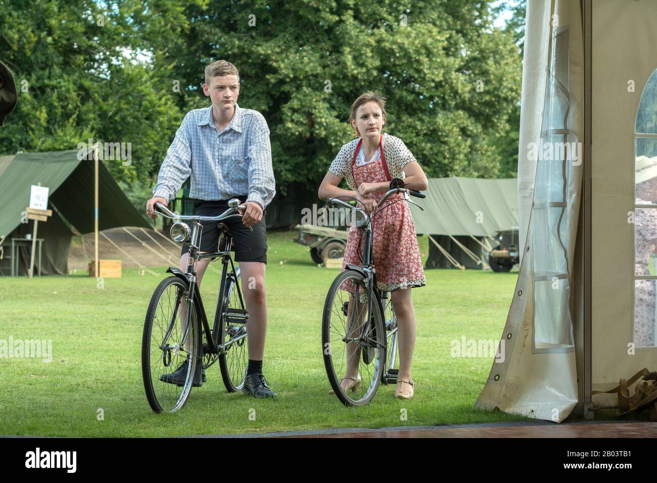 teenagers on Old grandad bikes stop and look into tent WWII dress costume reenactment World War II girl and boy on old bicycles Stock Photo