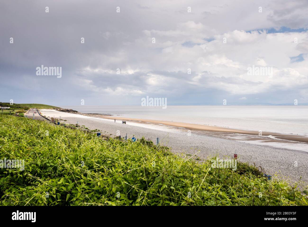 The long stony beach at The Knap, Barry, with sand exposed by the shoreline due to the low tide. The scene is calm,  sun shines between broken cloud. Stock Photo