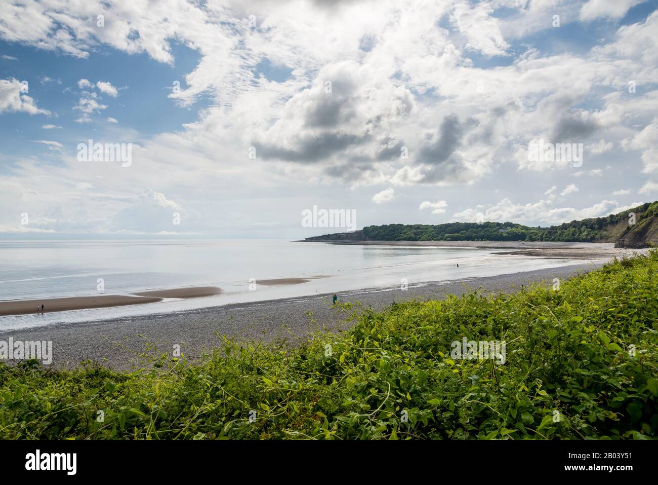 The long stony beach at The Knap, Barry, with sand exposed by the shoreline due to the low tide. The scene is calm,  sun shines between broken cloud. Stock Photo