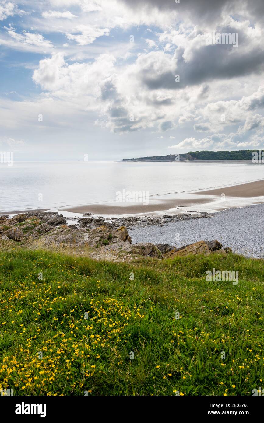 The long stony beach at The Knap, Barry, with sand exposed by the shoreline due to the low tide. The scene is calm,  sun shines between broken cloud. Stock Photo