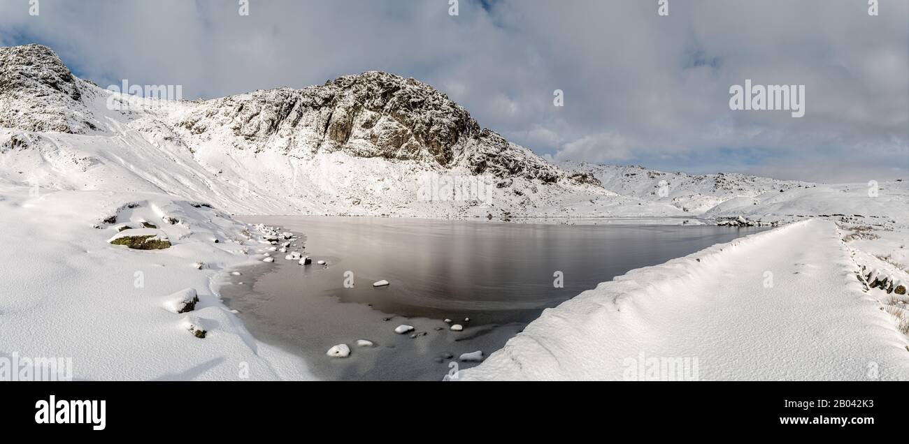 Pavey Arc towering over a frozen Stickle Tarn and the dam covered in fresh deep snow Stock Photo