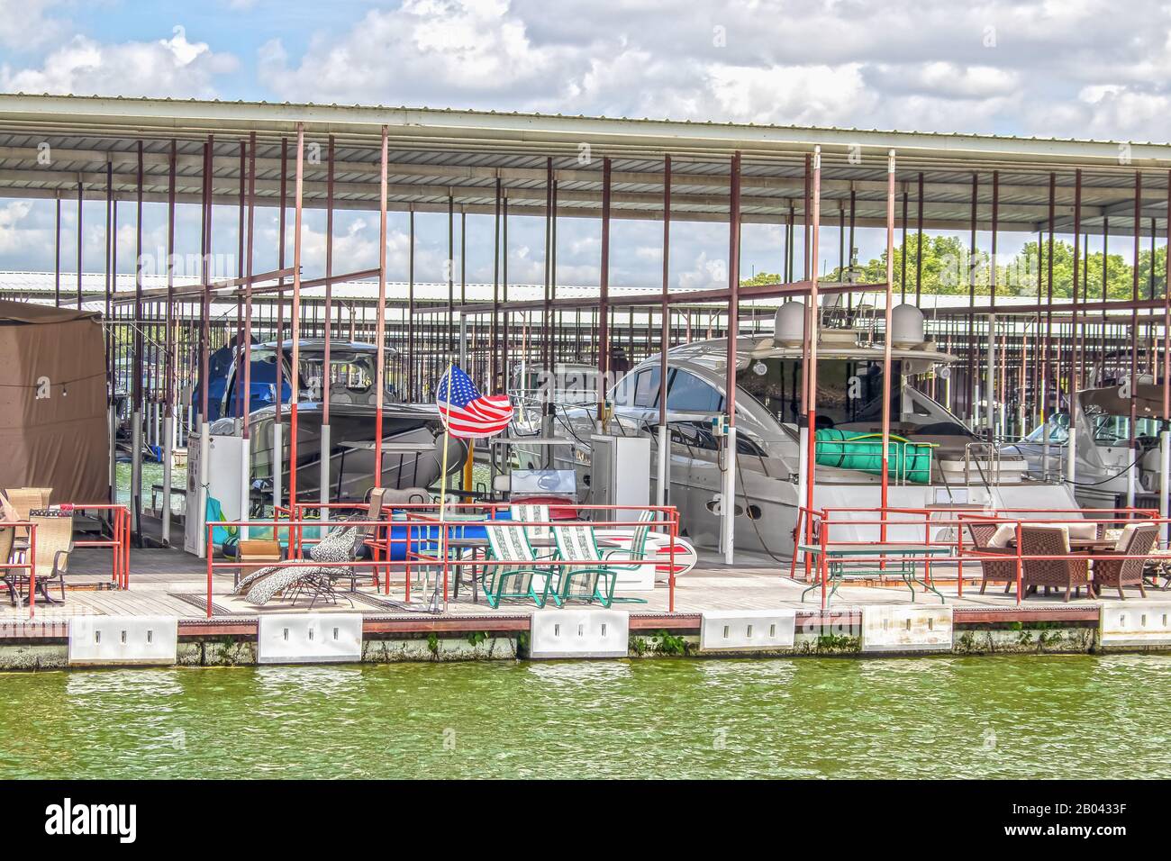 Party-boat covered dock on lake with expensive luxury speedboats docked and chairs and tables and toys for fun and guests in outside area Stock Photo