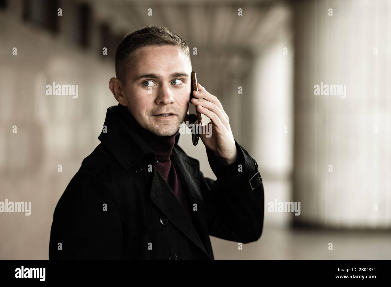 Stylish man in black trench coat and polo talking on a cell phone Stock Photo