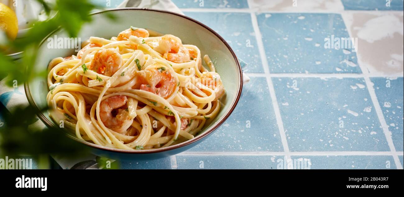 Panorama banner with Italian pasta and fresh grilled scampi served on a blue tiled surface in summer with copy space viewed past green herbs Stock Photo