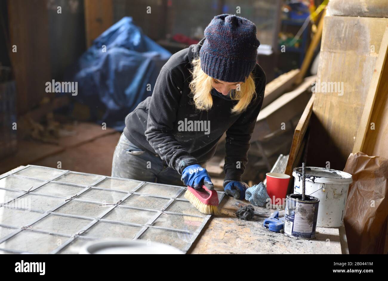 Woman stained glass working cleaning panel of clear glass on old building restoration. Working on site. Stock Photo