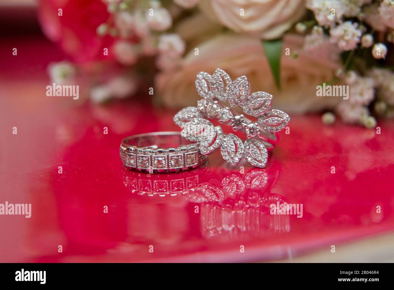 White wedding rings . flower bouquet selective focuse .Two silver wedding rings red background . Romantic and lovely wedding , macro . Bride and groom Stock Photo