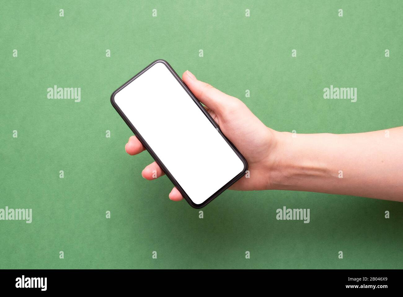 Female hand holding a blank screen mobile phone over green background ...