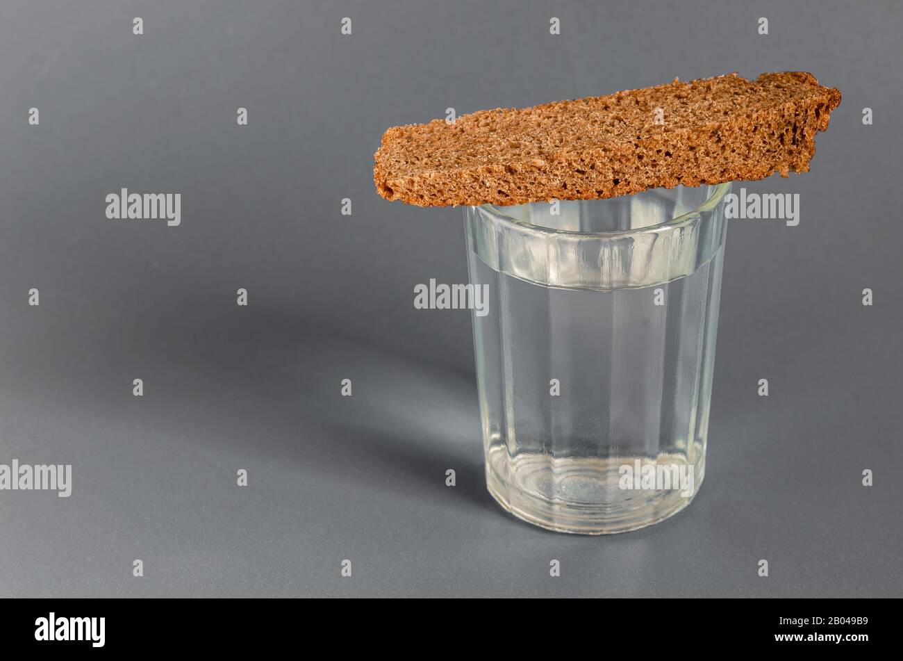 Full faceted glass of strong alcohol and bread on a gray background. Calm colors. Close-up. Selective focus. Stock Photo