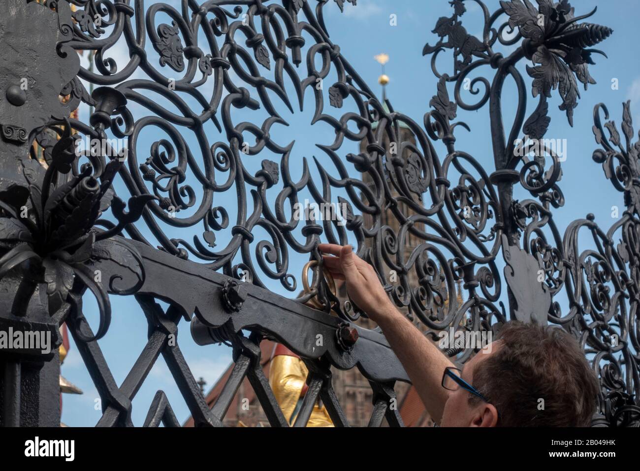Visitor rubbing a 'lucky' brass ring on the fence that surrounds the Schöner Brunnen (Beautiful Fountain) in Nuremberg, Bavaria, Germany. Stock Photo