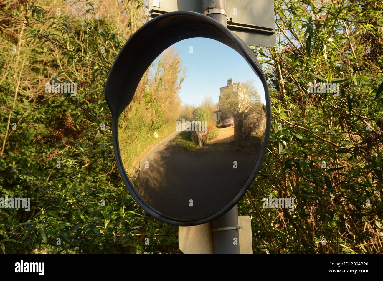 Convex mirror on signpost for observing oncoming traffic at a sharp corner. It shows the road ahead is clear. Stock Photo