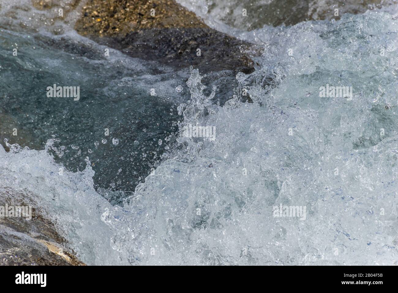A close-up of a wave splashing over the mountain river cascade boulders: full frame stop motion shot Stock Photo
