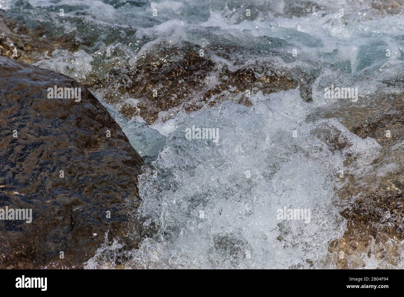 A close-up of a wave splashing over the mountain river cascade boulders: full frame stop motion shot Stock Photo