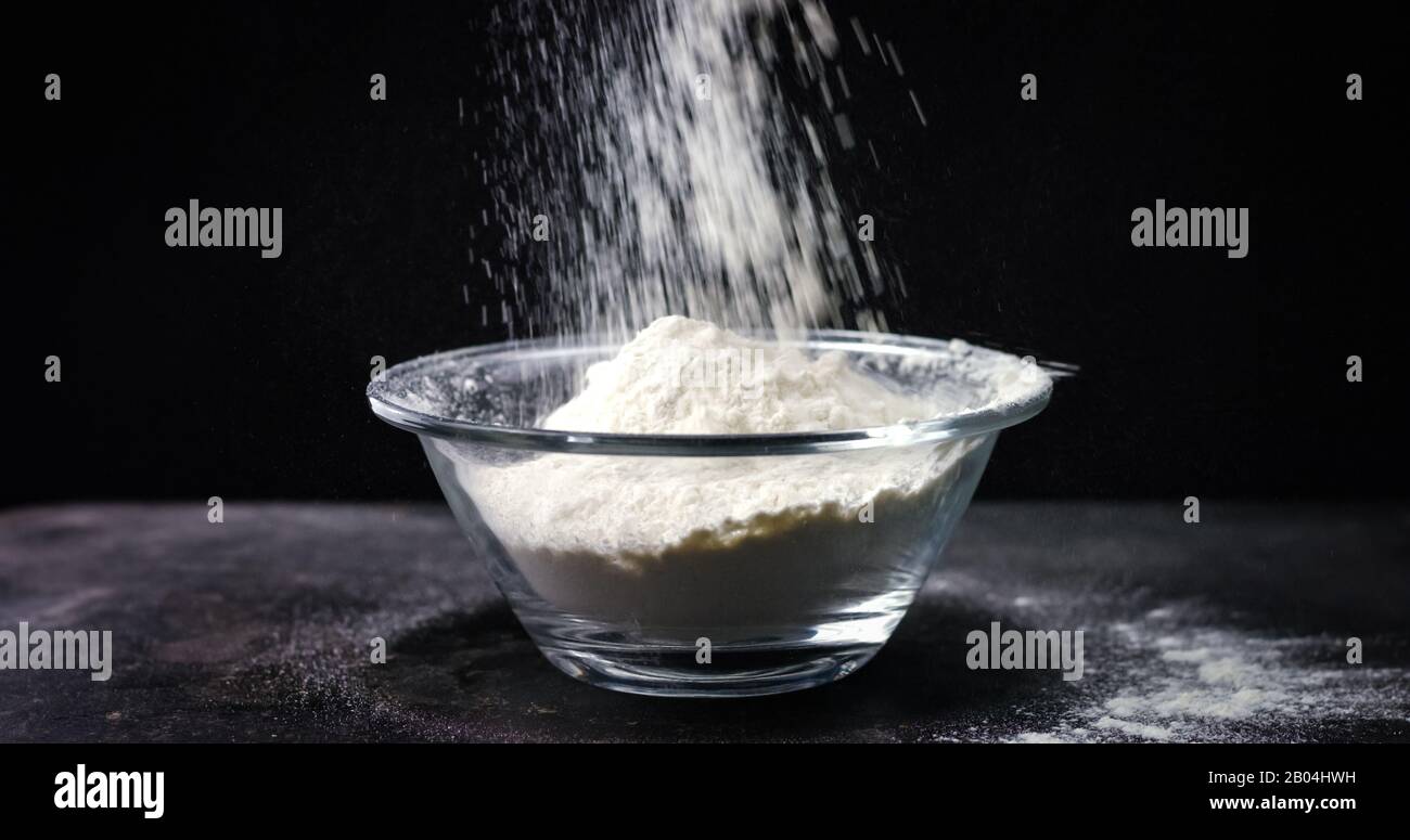 Flour is falling into a bowl in slow motion on black background Stock ...