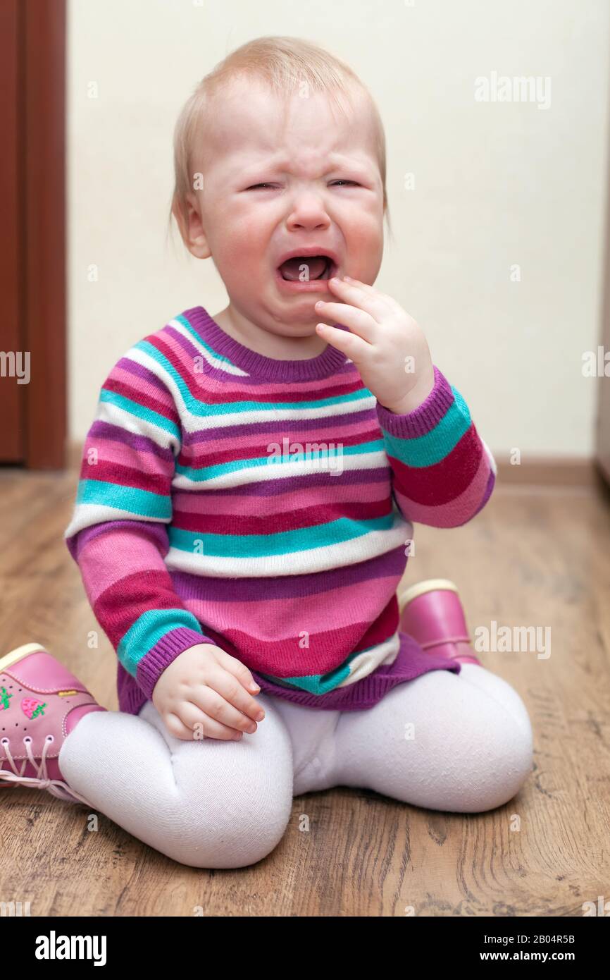 Portrait of crying baby girl in purple dress on living room at home Stock Photo Alamy