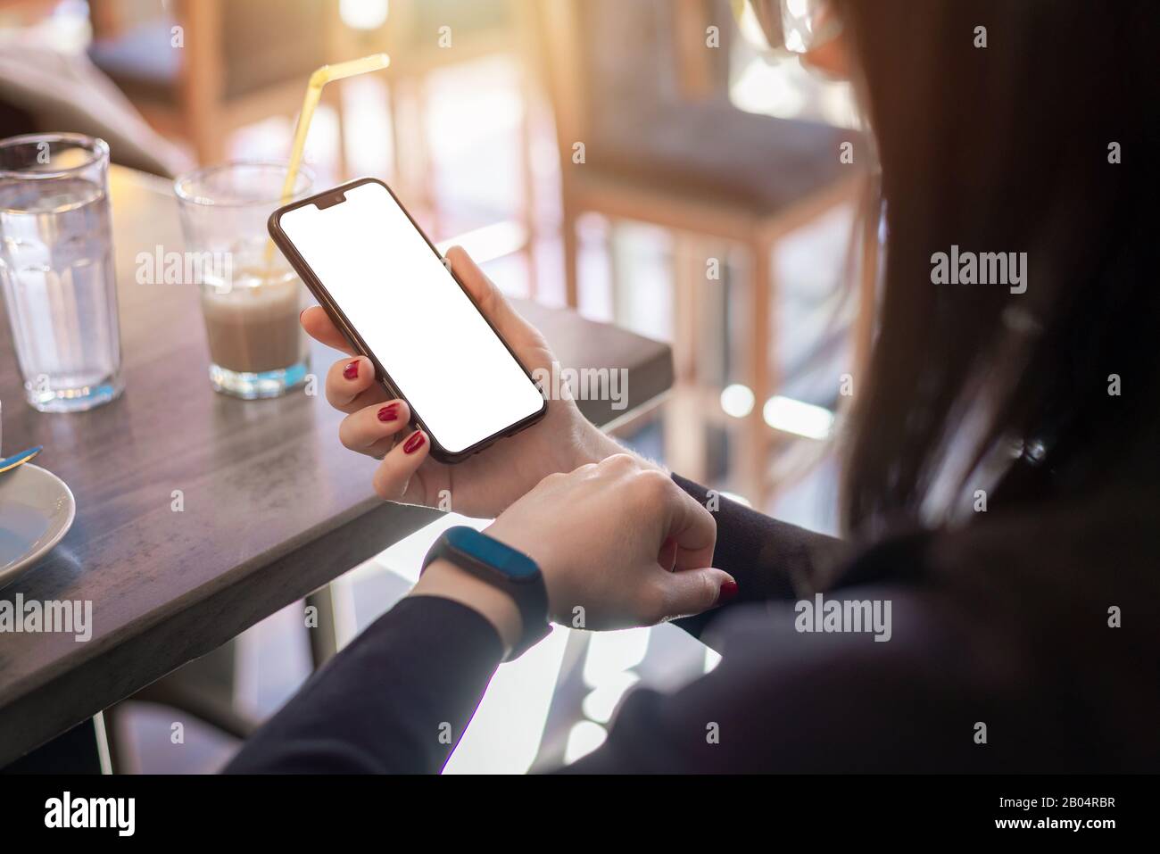 Woman watching smart phone and smart bracelet. hone with blank screen for mockup. Coffee sho in background Stock Photo