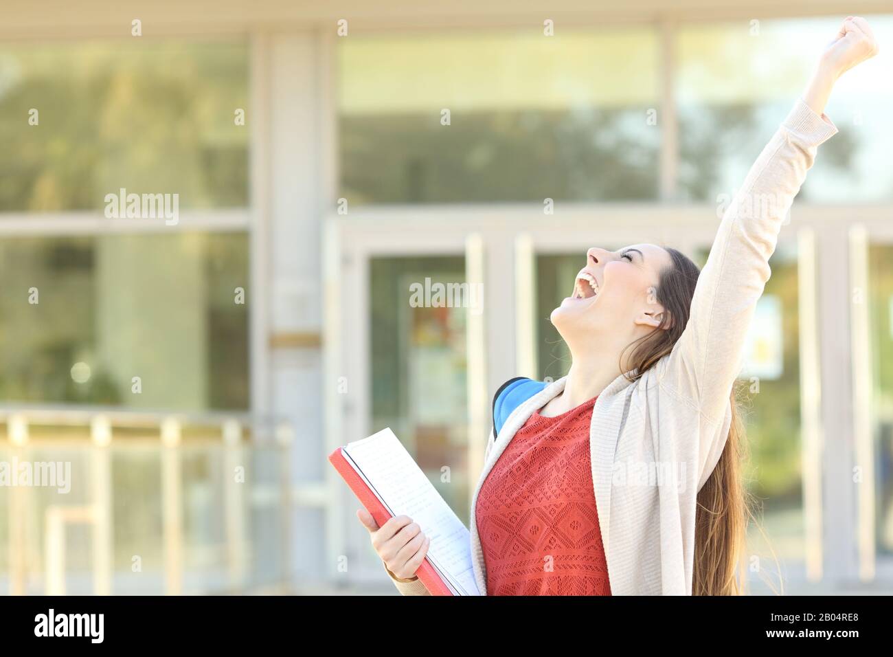 Excited student celebrating good grades raising arms standing in a college Stock Photo