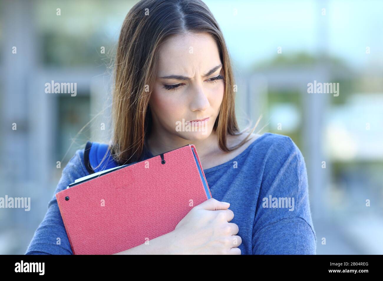 Front view portrait of a sad student looking down embracing folders