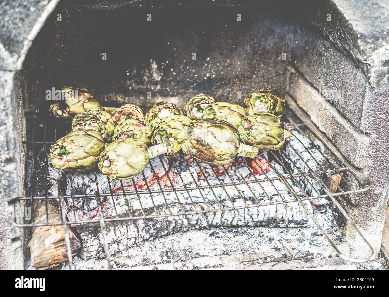 Cooked stuffed artichokes on wood barbecue grill - Vegetarian tasty dinner outdoor with friends - Focus on bottom right vegetables - Vintage contrast Stock Photo