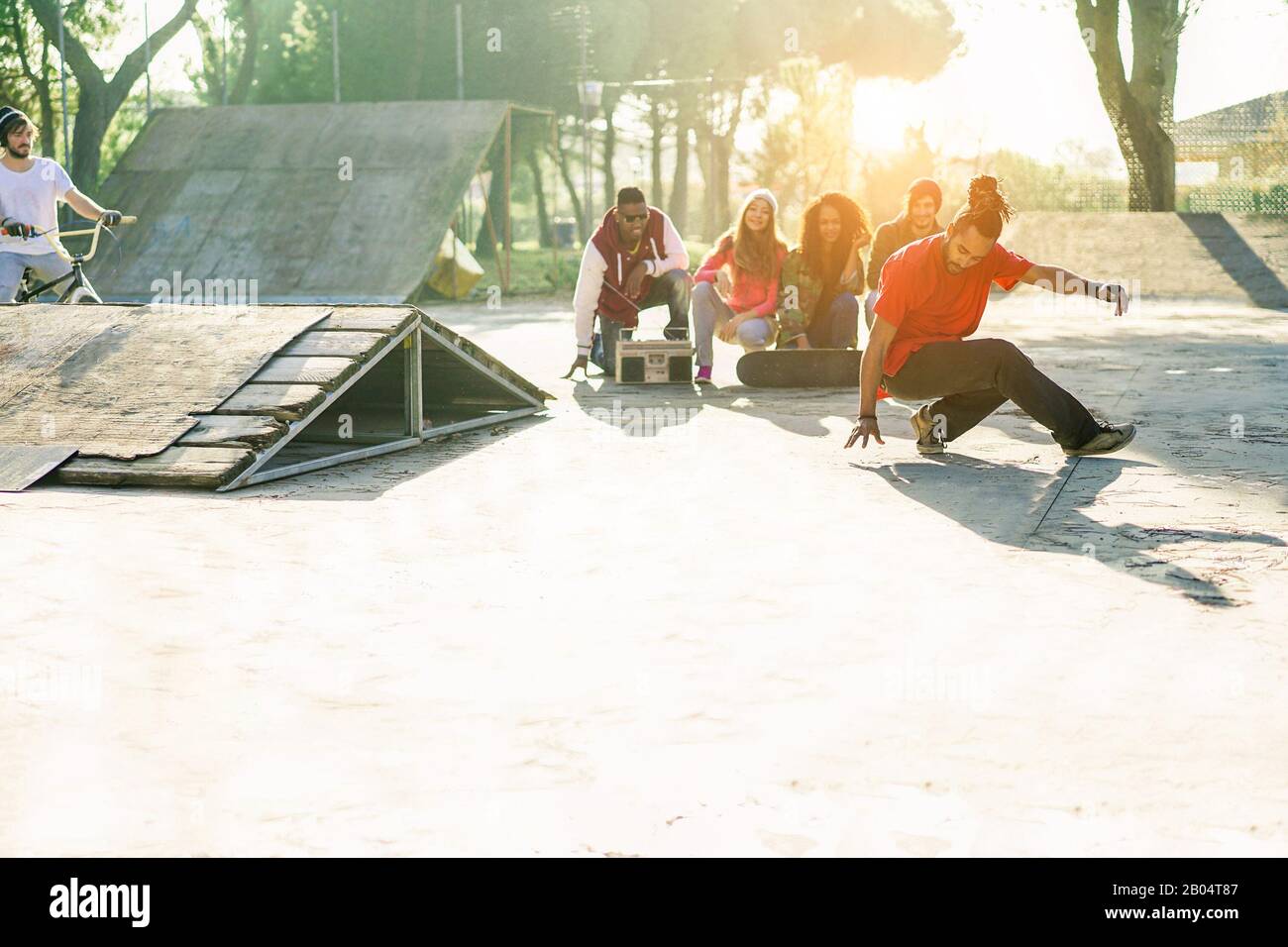 Group of happy friends listening music and watching breakdancer perfoming in city skate park - Young people having fun - Hip hop lifestyle concept - F Stock Photo