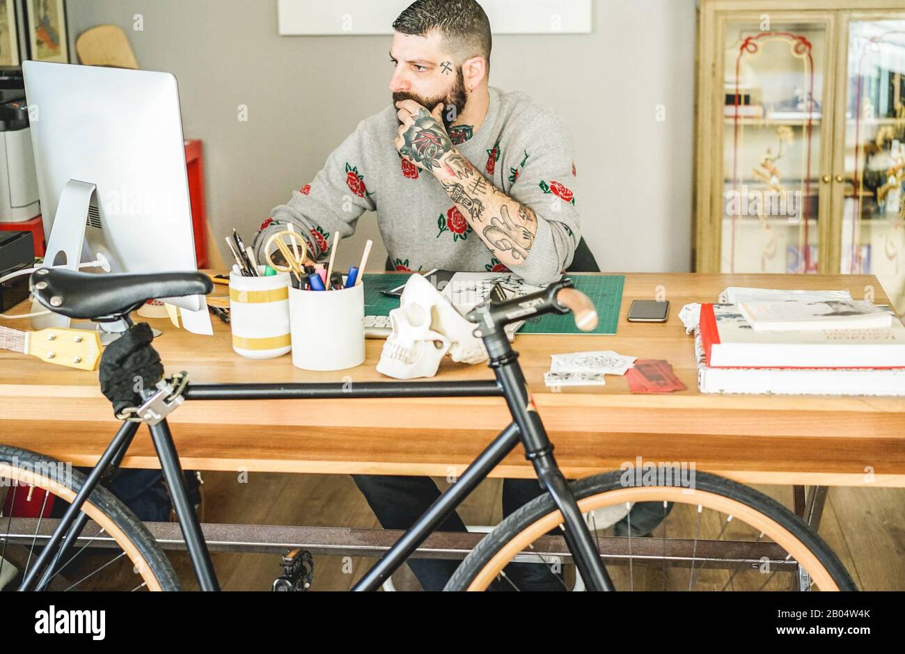 Tattooed artist using computer inside ink studio - Hipster tattoer working on new project - Fashion, arts and trends concept - Focus on man face Stock Photo