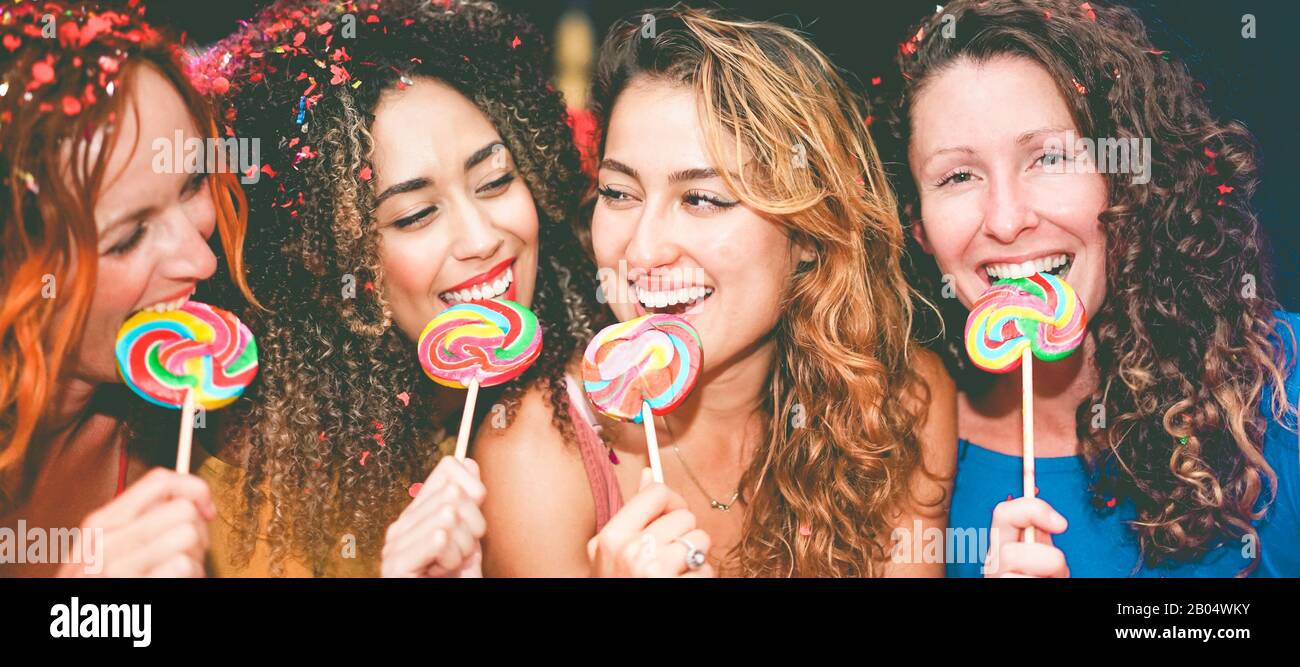 Happy young girls eating candy lollipop at party in night disco club - Millennials women having fun together - Youth, generation trends, female friend Stock Photo