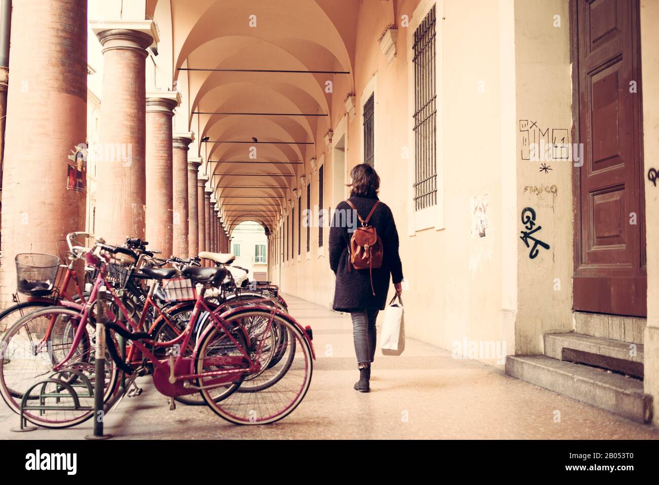 Woman walking next to vintage bikes under Bologna porticoes covered footpath in the  historical medieval centre of Bologna. Emilia-Romagna, Italy. Stock Photo