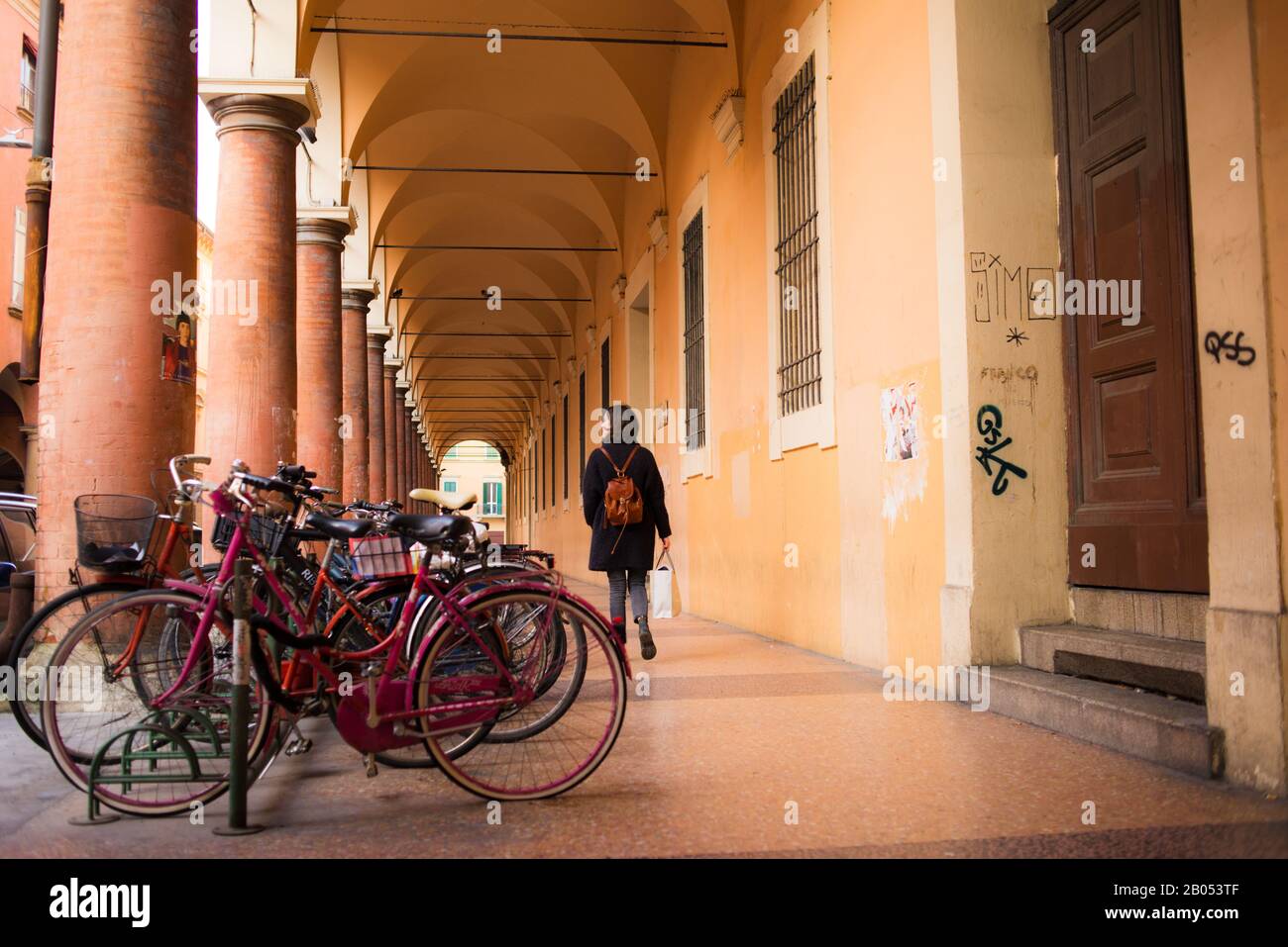 Woman walking next to vintage bikes under Bologna porticoes covered footpath in the  historical medieval centre of Bologna. Emilia-Romagna, Italy. Stock Photo