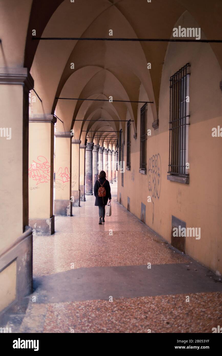 Woman walking alone under Bologna porticoes covered footpath in the  historical medieval centre of Bologna city. Emilia-Romagna region, Northern Italy Stock Photo