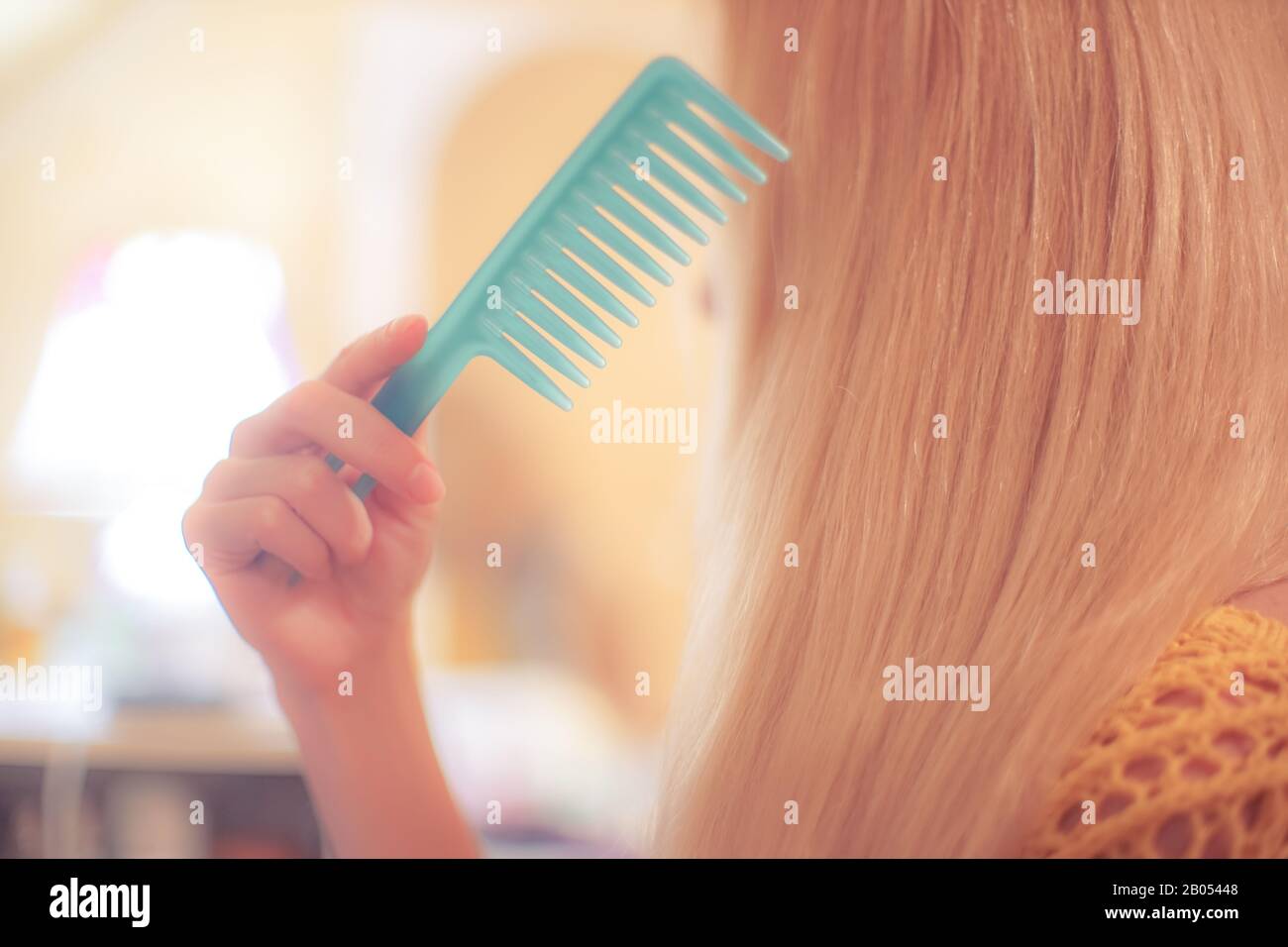 Blonde girl combing her long hair with a thin blue comb. Girls daily care Stock Photo