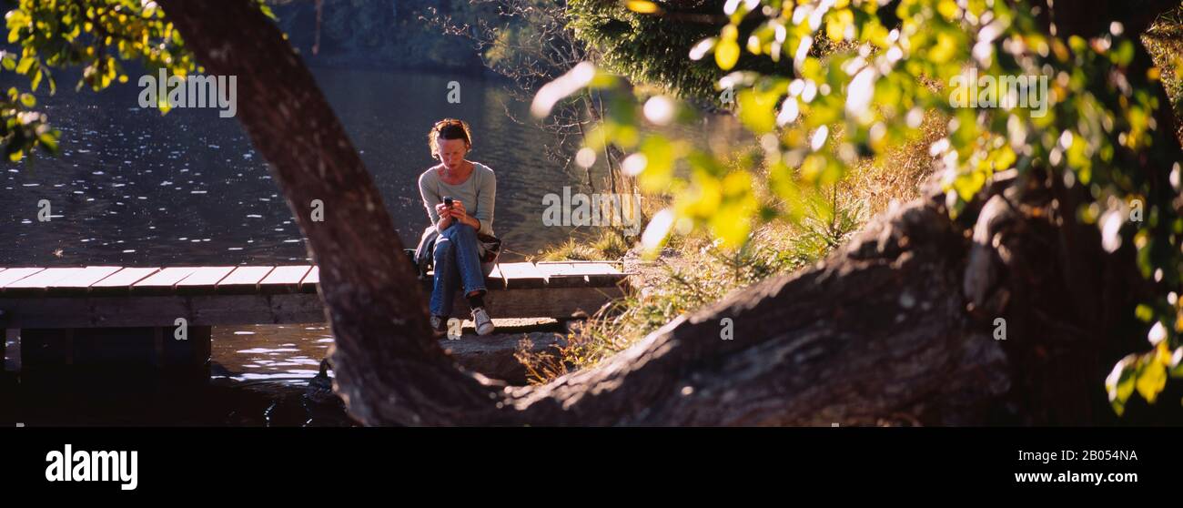 Woman sitting on a foot bridge and using a mobile phone, Northern Black Forest Region, Baden-Wurttemberg, Germany Stock Photo
