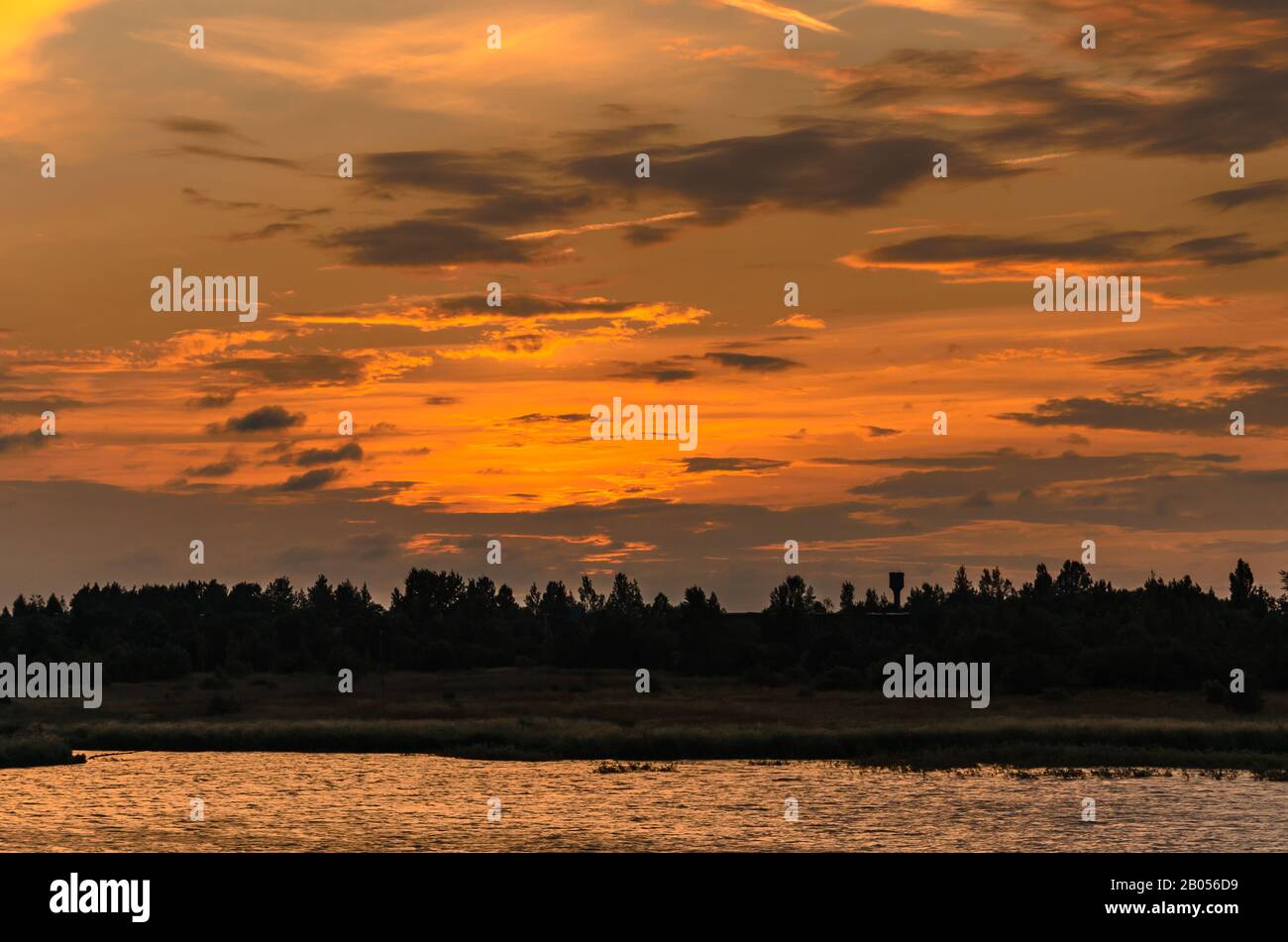 Sunlit clouds over the forest and river after sunset Stock Photo