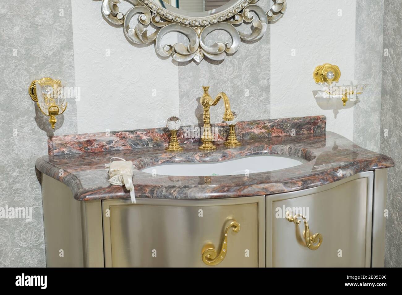 Interior in the bathroom, vintage mirror and expensive marble washbasin, stainless steel tub, with gold handles close-up. Stock Photo
