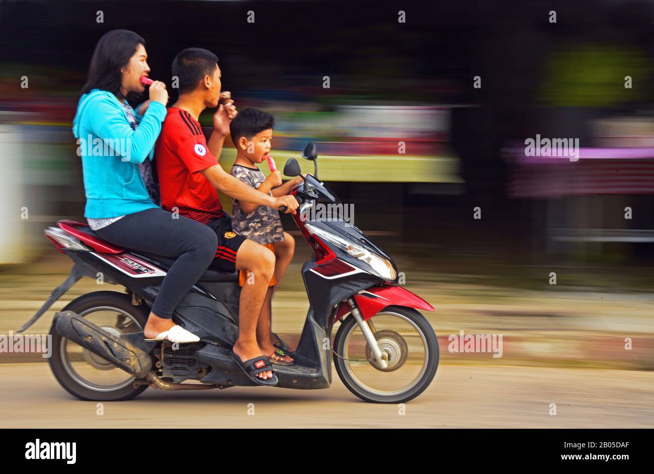 three people on the same motor bike sucking ice cream, Thailand, Phuket Stock Photo