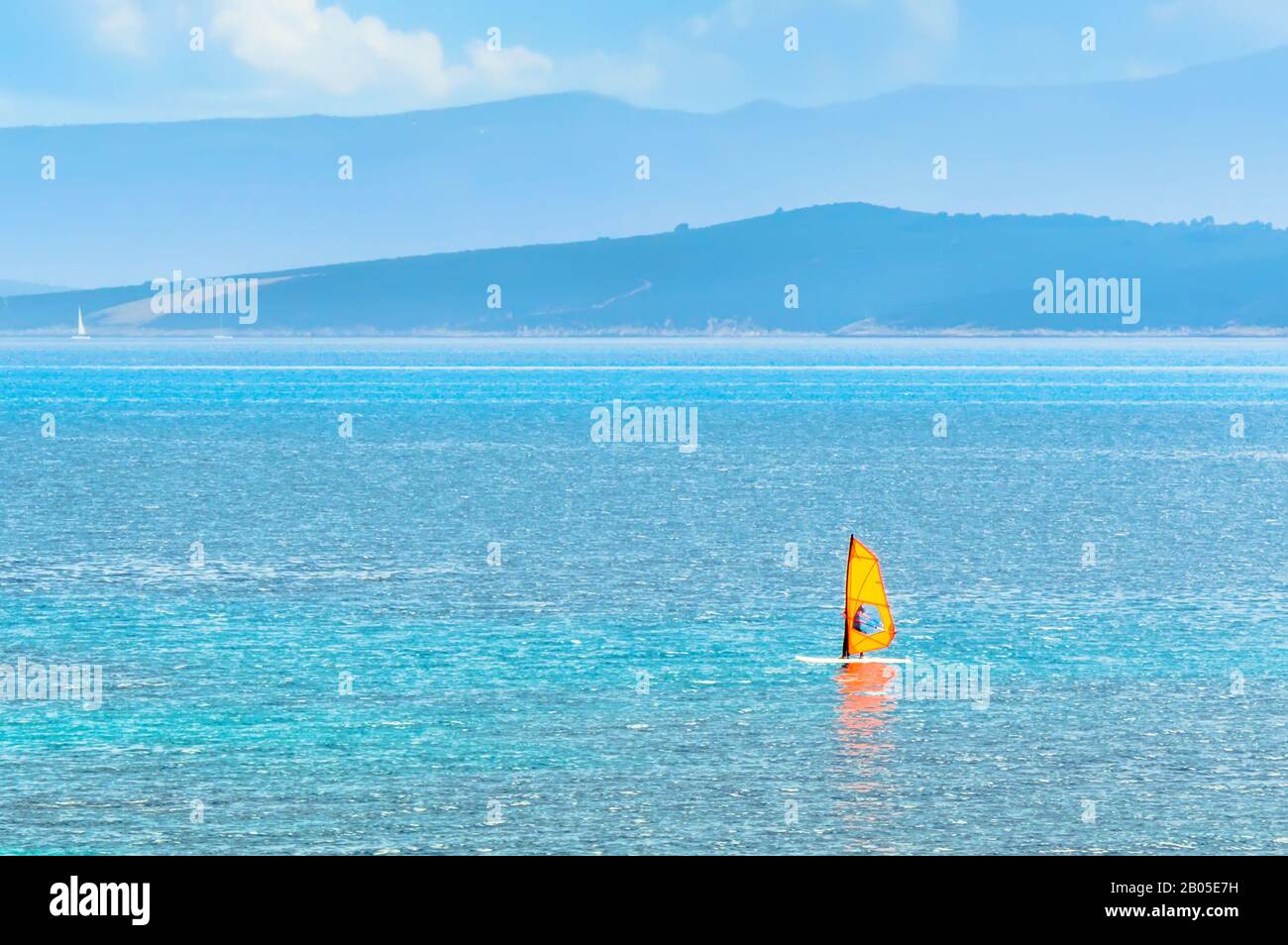 Windsurfer on yellow sailboard in Adriatic Sea in Bol on Brac Island near Split, Croatia. Water sports windsurfing in turquoise water and mountains in Stock Photo