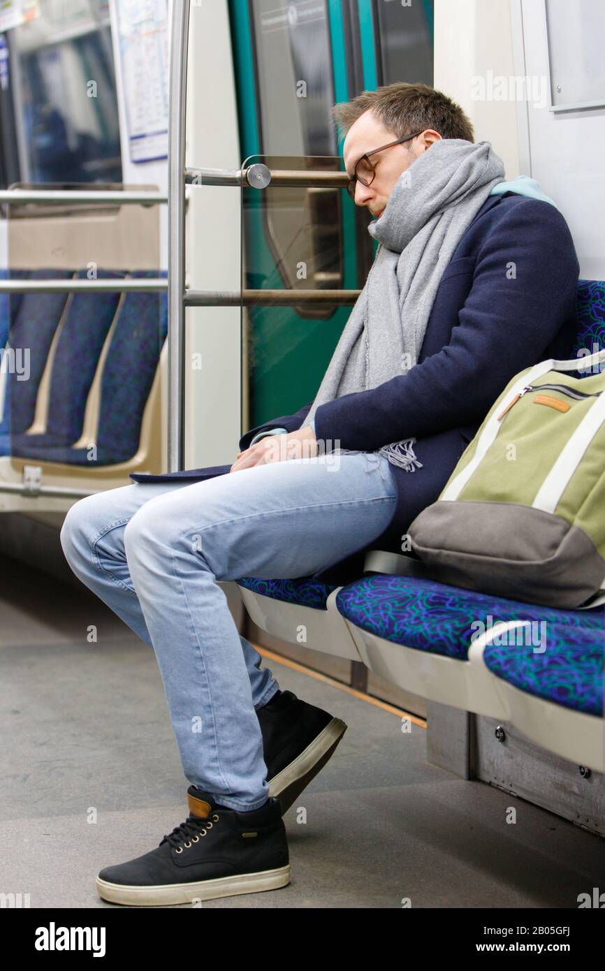 Tired man in eyeglasses in metro train. Young exhausted male sleeping in subway after work, soft focus. Chronic fatigue, sleep deprivation concept. Stock Photo