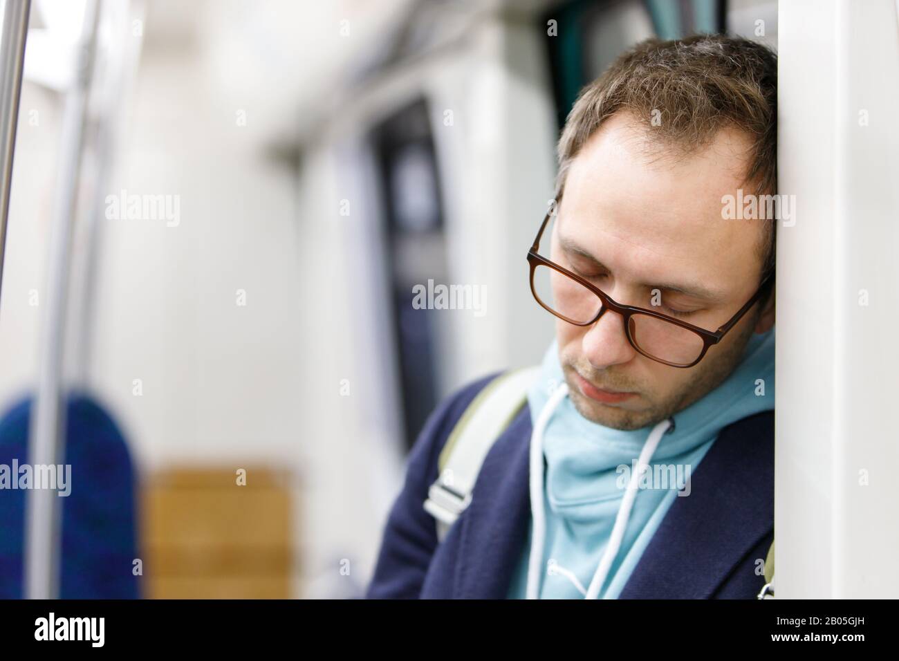 Tired man in glasses in metro train. Young exhausted male standing and sleeping in subway after work, soft focus. Chronic fatigue, sleep deprivation Stock Photo