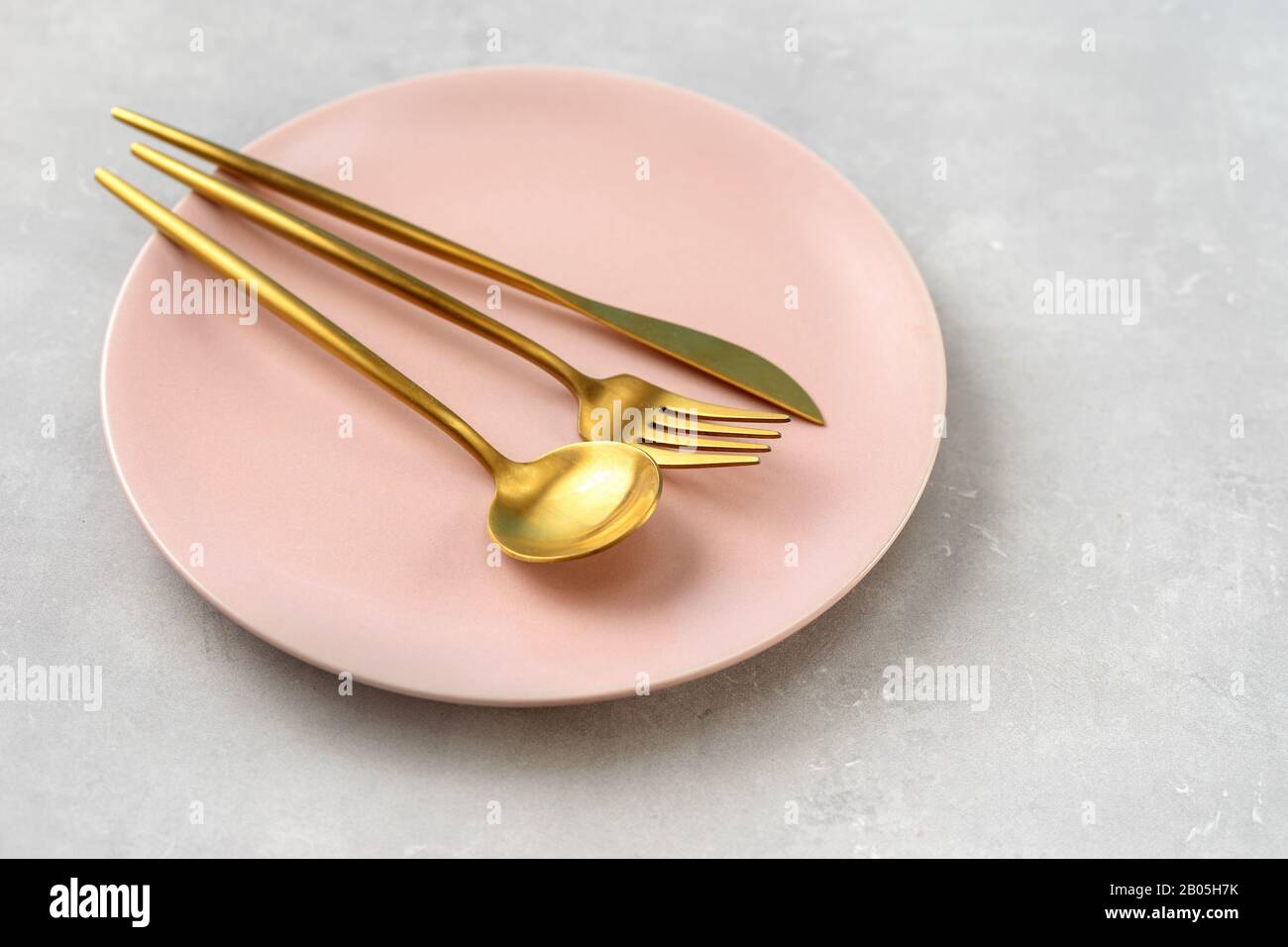 Beautiful pink plate and gold cutlery on grey background Stock Photo