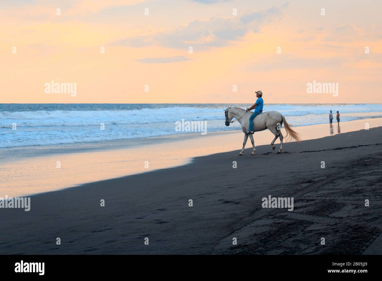 man riding a white horse on the beach during sunset Stock Photo