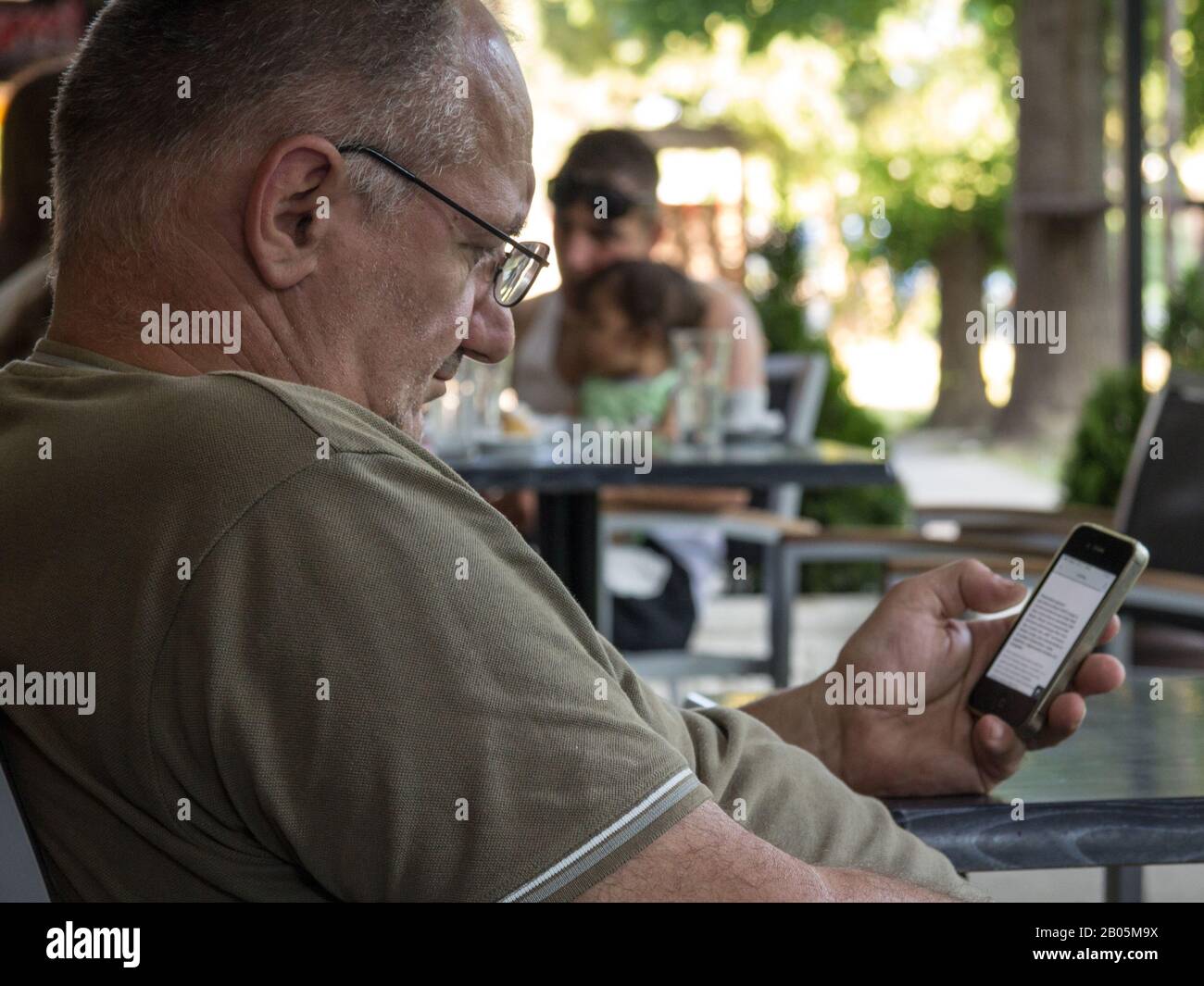 ALIBUNAR, SERBIA - JUNE 6, 2015: Oldd sernior white man sitting in a cafe looking at an Apple IPhone 4 smartphone using the mobile internet data.   Pi Stock Photo
