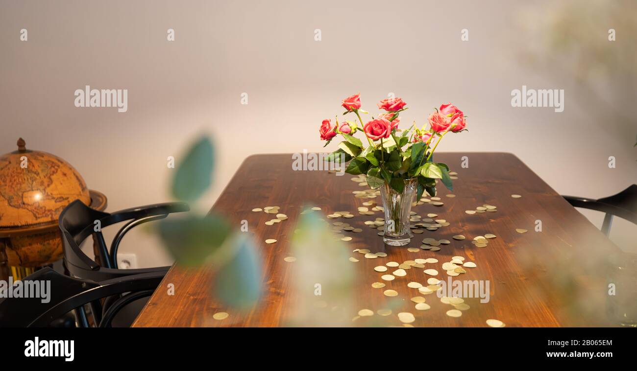 Vase with red roses on a table with gold confetti and a globe in the corner. Stock Photo