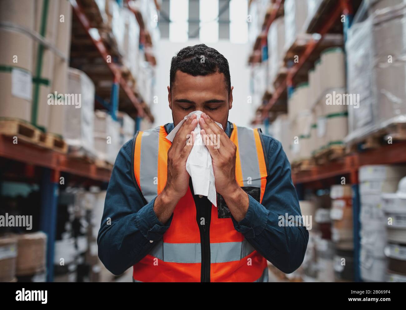 Young sick african warehouse worker blowing nose while working wearing safety vest Stock Photo